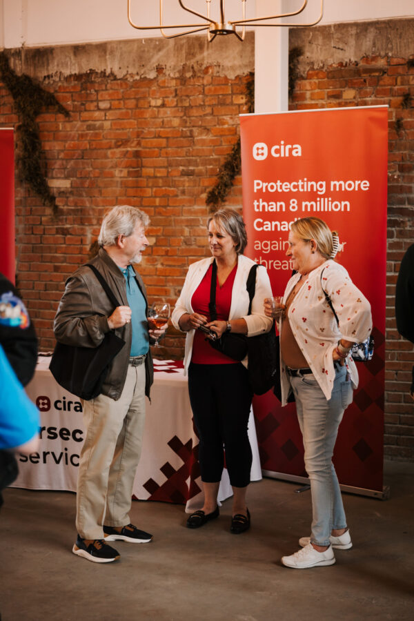 Three people smiling and talking in front of a banner at Canadians Connected: Edmonton