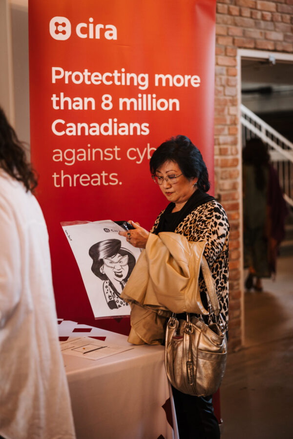 A woman holding a caricature drawing of herself in front of a Canadians Connected: Edmonton sign
