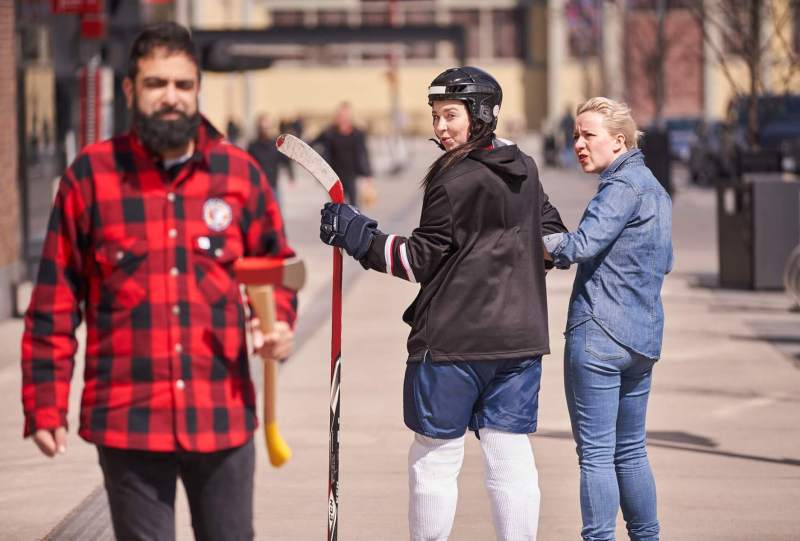 Hockey player checks out lumberjack while woman in Canadian tuxedo looks on in disbelief